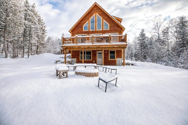 Eine Blockhütte mit Balkon, umgeben von schneebedeckten Bäumen.