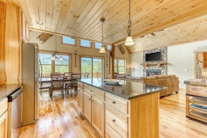 A spacious kitchen with wooden cabinetry, a central island, and a dining area with a table and chairs. - The Escape at ThunderSnow Sunday River lodge with Stunning Views to Wake Up to (Bethel)