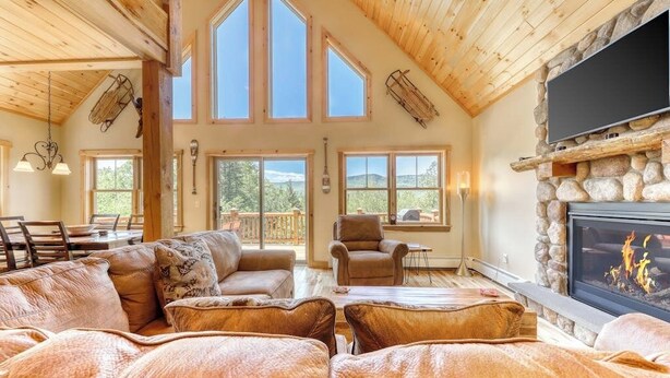 Un salón amplio con sofás de cuero, chimenea de piedra, televisor de pantalla plana y ventanas grandes.