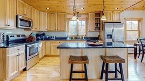 Una cocina con armarios de madera, electrodomésticos de acero inoxidable, una isla central con taburetes e iluminación colgante.