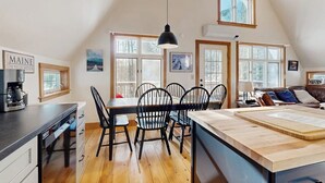Une cuisine équipée d’une table à manger, de chaises, d’une machine à café et d’une grande fenêtre.