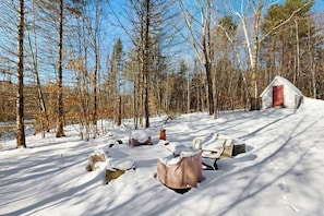 Un espace extérieur enneigé comprenant une petite cabane, un foyer et des rochers éparpillés.
