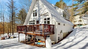 Une maison blanche avec une terrasse en bois et une cour enneigée.