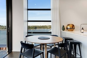 Un espace repas moderne avec une table ronde, des chaises noires, une vue sur la mer et une grande fenêtre.