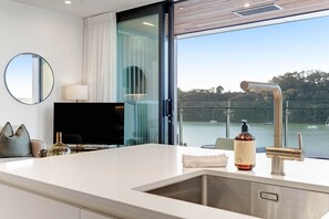 A modern kitchen with a large window, a sink, and a bottle of liquor. - Catalina Bay Waterfront Retreat | Views & Carpark (Auckland West)