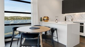 Et moderne køkken med en marmorbordplade, et rundt spisebord med stole, og udsigt til havet med sejlbåde.