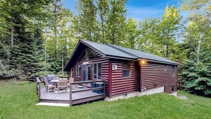 Una cabaña de troncos con un balcón, mobiliario exterior y vistas del bosque circundante.