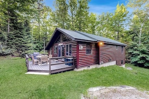 Eine Blockhütte mit einer Terrasse, Sitzgelegenheiten im Freien und Blick auf den umliegenden Wald.