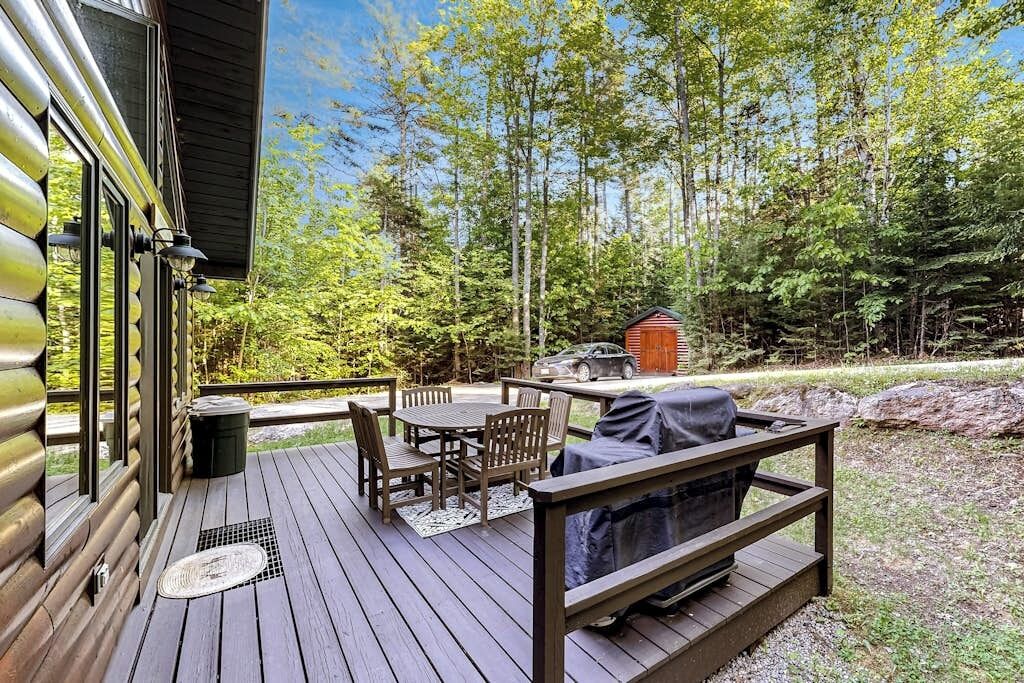 A wooden deck with outdoor furniture, a grill, and a view of a forested area.