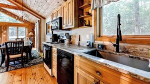 Interior de una cabaña de madera con cocina, comedor y vistas al bosque.