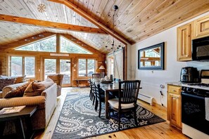 Ein gemütliches Blockhaus-Interieur mit Essbereich, Küche und großem Fenster mit Blick auf einen Wald.