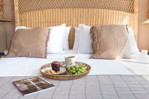 Ein Bett mit gewobener Kopfteil, weißer Bettwäsche und einem Tablett mit Trauben, Keksen und einer Tasse.