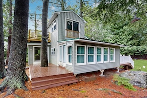 Une maison à deux étages avec une terrasse, entourée d’arbres.