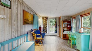 Een kamer met een houten lambrisering, een blauwe bank, een rieten stoel, een groene stoel, een blauwgroene bureau en een boekenkast.