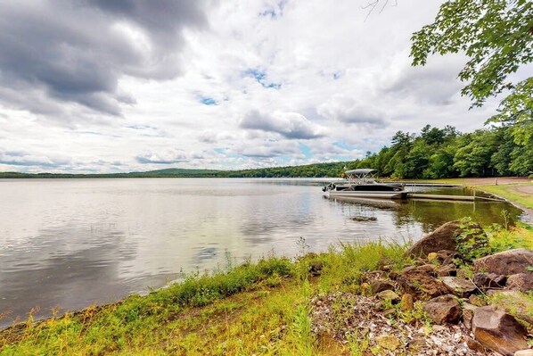 A calm lake with a dock, surrounded by greenery and a cloudy sky.