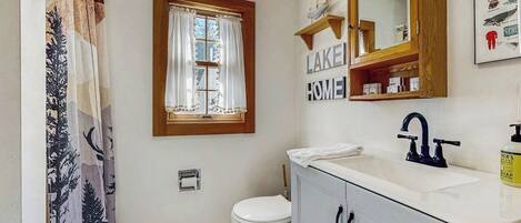 A bathroom with a white sink, a mirror, a window with curtains, and a toilet.