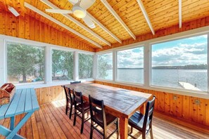 Eine Holzhütte mit einem großen Esstisch, vier Stühlen und Blick auf einen See.