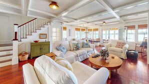 A spacious living room with a staircase, multiple seating areas, and large windows. - Lakefront home with private dock, kayaks, firepit, grill, & sunroom (Monmouth)