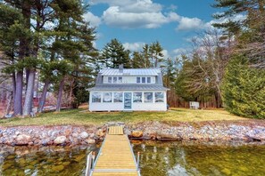 Ein Haus mit Steg, der zu einem Teich führt, umgeben von Bäumen.