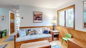 Une pièce chaleureuse avec un canapé en bois, une petite table, une chaise, une lampe et une grande fenêtre.