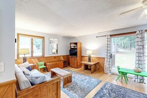 Ein gemütliches Wohnzimmer mit einer Couch, einem Fernseher, einem kleinen Tisch und einem Fenster mit Vorhängen.