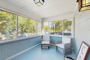 Ein Wintergarten mit großen Fenstern, Korbstühlen und einer Deckenleuchte.