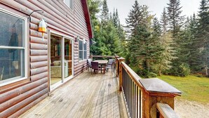 A log cabin with a deck, outdoor furniture, and a view of the surrounding forest. - Dog-friendly Sunday River retreat with large yard, grill, washer/dryer (Bethel)