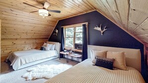 A cozy cabin with two beds, a ceiling fan, a window with curtains, and a fur rug. - Dog-friendly Sunday River retreat with large yard, grill, washer/dryer (Bethel)