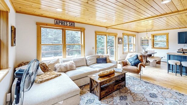 A cozy living room with a large sofa, a coffee table, and a fan. There is a sign that reads 'APRES SKI' on the wall. - Dog-friendly Sunday River retreat with large yard, grill, washer/dryer (Bethel)