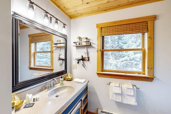 Un baño con un espejo grande, un lavamanos, una ventana con vistas a árboles y un perchero.