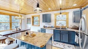 A kitchen with wooden ceiling, granite countertops, blue cabinets, stainless steel appliances, and large windows. - Dog-friendly Sunday River retreat with large yard, grill, washer/dryer (Bethel)