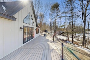 Una casa moderna con una terrazza in legno, ampie finestre e vista su un paesaggio innevato.