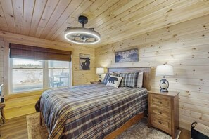 Une chambre à coucher aux murs lambrissés, avec un lit, des lampes de chevet, une fenêtre et un tableau accroché au mur.