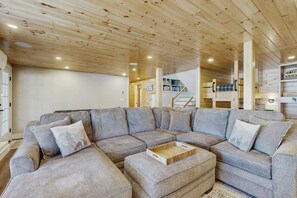 Un salon moderne avec un canapé d’angle, un plafond en bois et un escalier en arrière-plan.