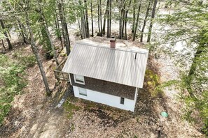 Eine kleine, eingeschossige Holzhütte mit einer Metalldecke, umgeben von Bäumen.