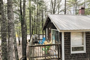 Eine Holzhütte mit einer Holzterrasse, einem Schornstein und einer Glastür, die auf eine Veranda mit Gartenmöbeln führt.