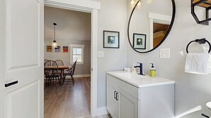 A bathroom with a white vanity, a round mirror, and a towel rack.
