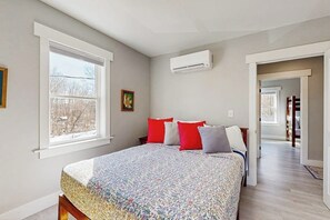 Un dormitorio con cama, ventana, aire acondicionado y puerta que da a otra habitación.