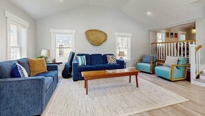 A spacious living room with a blue sofa, a wooden coffee table, and a large woven wall hanging.