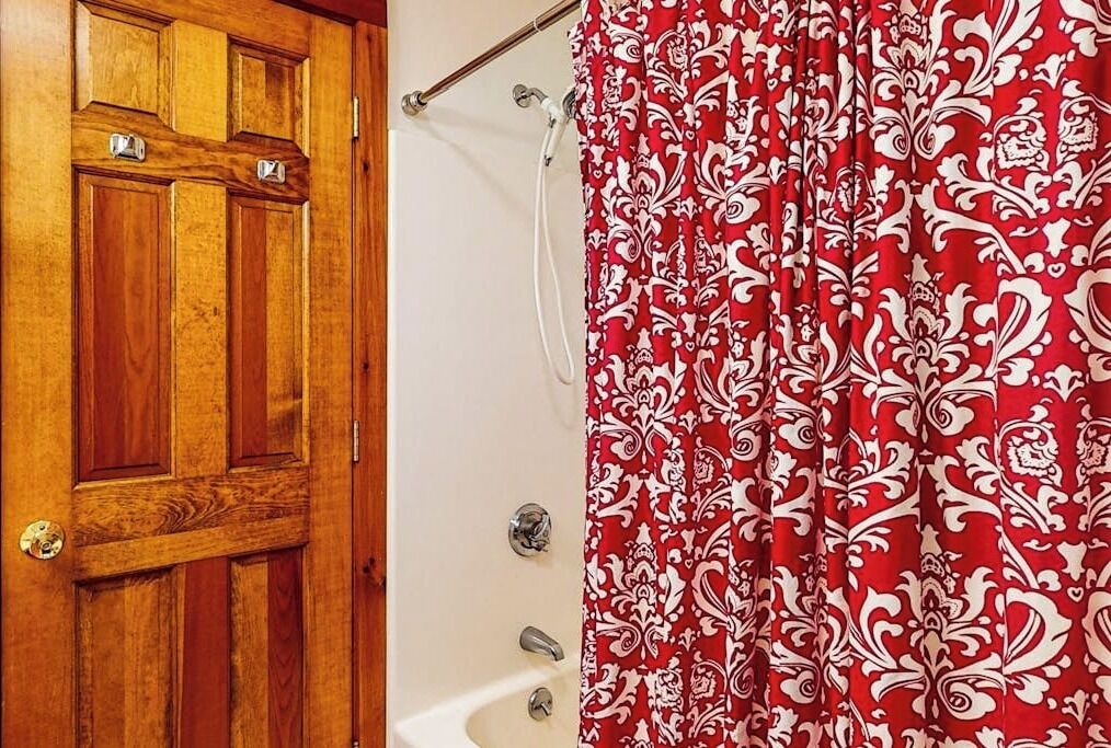 A wooden door and a bathroom with a red patterned shower curtain.