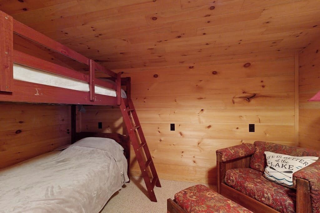 Eine Holzhütte mit einem Doppelstockbett, einer Himmelsleiter, einer kleinen Couch und einem Kissen mit Schrift.