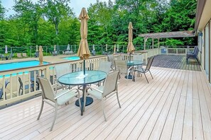 Une terrasse en bois avec une piscine, des sièges d’extérieur et des parasols.