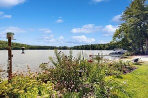 Blick auf einen See mit Bootssteg, Vogelhaus und üppiger Vegetation.
