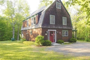 A two-story wooden house with a red door, a front porch, and a gravel driveway. - Spacious river home w/ pellet stove, outdoor dining area, fire pit, & BBQ grill (Litchfield)