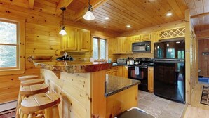 Ein Holzblockhaus-Interieur mit einer Küche, die Holzschränke, eine Granitabdeckung, einen Kühlschrank und eine Mikrowelle zeigt.
