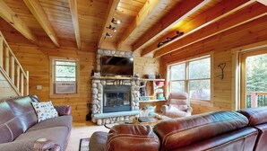 Ein Holzblockhaus-Interieur mit Kamin aus Stein, Ledersofas und großen Fenstern.