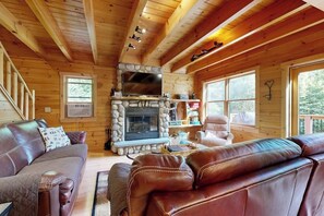 Ein Holzblockhaus-Interieur mit Kamin aus Stein, Ledersofas und großen Fenstern.