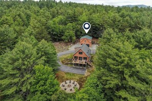 Eine Lodge, umgeben von dichtem Wald, mit einer runden Sitzgruppe und einer Treppe, die zum Hauptgebäude führt.