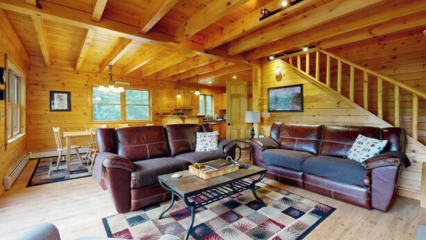 Ein rustikales Blockhaus-Interieur mit einer Holztreppe, Ledersofas, einer Essecke und einer Küche.