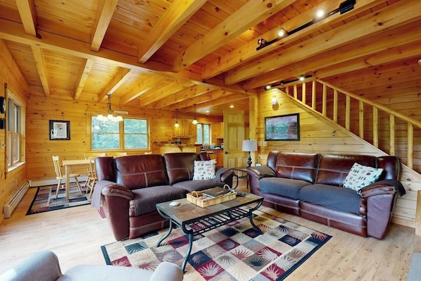 Ein rustikales Blockhaus-Interieur mit einer Holztreppe, Ledersofas, einer Essecke und einer Küche.